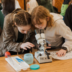two grils looking into a microscope at a water sample